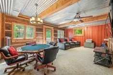 Cozy rustic game room with poker table, leather reclining chairs, corrugated metal ceiling, and wooden walls.