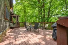 Spacious wooden deck with outdoor furniture surrounded by lush green trees.