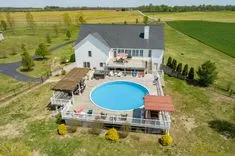 Aerial view of a two-story house with a swimming pool and patio area, surrounded by open fields.