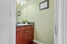 Small bathroom with a red vanity cabinet, wall-mounted mirror with overhead lighting, and green walls.