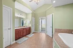 Spacious bathroom interior with tan tiled flooring, a large vanity with redwood cabinets and dual sinks, a wide mirror, and a separate tub and shower area.
