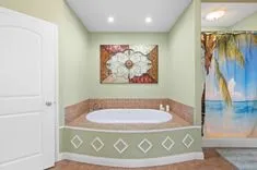 Spacious bathroom with a corner jacuzzi tub, decorative tiling, and a tropical mural wall painting.