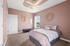 Spacious bedroom with a queen-size bed, pastel walls, a ceiling fan, and a sliding door leading outside.