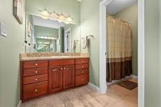 A bathroom interior with a large mirror, double sink vanity with wooden cabinets, and a shower curtain in the background.