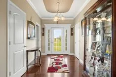 Elegant hallway interior with a wooden floor, red runner rug, white walls, a glass-fronted display cabinet, and a front door with sidelight windows.