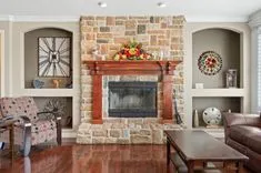 Cozy living room with stone fireplace, wood mantel decorated with a fruit garland, and assorted decorative items on adjacent built-in shelves.