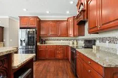 Modern kitchen interior with cherry wood cabinets, stainless steel appliances, and granite countertops.