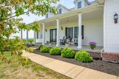 Charming white house with a covered porch, rocking chairs, and landscaped garden, path leading to a bright, welcoming entrance.