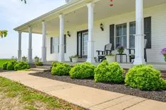 Traditional white porch with rocking chairs and neatly trimmed bushes along a stone walkway.