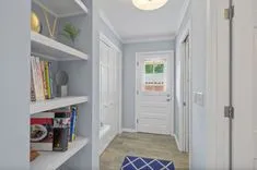 Bright hallway with built-in shelving units, decorative items, and a view of a door with a window showing greenery outside.
