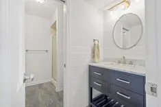 Modern bathroom interior with gray vanity cabinet, circular mirror, and walk-in shower.