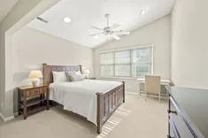 Bright spacious bedroom with a king-sized bed, large windows, and a ceiling fan.