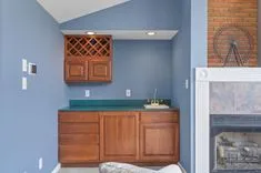 A cozy home corner featuring a wooden cabinet with a wine rack above, teal countertop, and a brick fireplace to the side with a glimpse of a glass door.