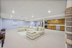 Spacious modern basement living area with sectional sofa and kitchenette in the background.