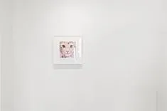 Small framed artwork hanging on a white wall in a minimalistic room setting.