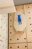 A blue cutout of a cat on an oval white board attached perpendicularly to a wall with a pegboard pattern.