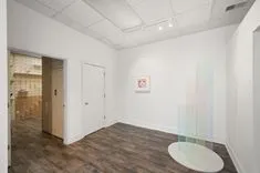 Interior of an empty room with wooden flooring, white walls, a closed door, and a single framed picture hanging on one wall.