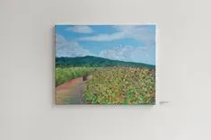 A canvas painting hanging on the wall depicting a rural landscape with a path through green fields under a cloudy blue sky.