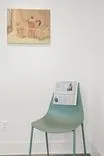 "Art gallery corner with a minimalist painting on the wall above a modern chair holding informational pamphlets"