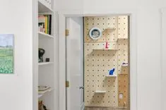 A DIY climbing wall inside a room with a white bookshelf on the left, viewed through an open door.