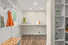 Modern home entrance with built-in white bench, shelving, hardwood floors, and decorative plants.