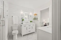 Modern white bathroom interior with double vanity, mirrors, toilet, and shower.