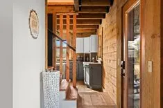 Rustic cabin interior with wooden walls and beams, a small kitchen area with cabinets, and a glass door leading outside.