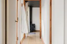 A view down a hallway with a white robe hanging on the left leading towards a black wood-burning stove at the end.
