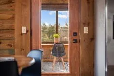 Wooden doorway open to a sunny view with a potted plant on a black mesh chair, rustic cabin interior details with a blurred foreground.