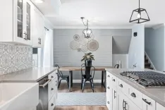 Modern kitchen interior with white cabinets, patterned backsplash, a wooden dining table with black chairs, and a pendant light.