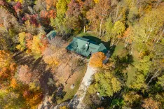Aerial view of a house with a green roof surrounded by trees with autumn foliage colors.