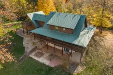 Aerial view of a large two-story cabin with green roofing, surrounded by autumn foliage.