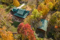 Aerial view of a house with a green roof surrounded by trees with autumn foliage colors.