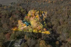 Aerial view of a secluded house surrounded by dense woods with autumn-colored foliage.
