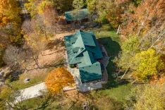 Aerial view of a residential home with a dark green roof surrounded by colorful autumn trees.