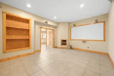 Spacious empty room with tiled flooring, wooden trim, a built-in shelf, and a large whiteboard on the wall.