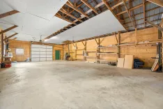 Spacious empty garage interior with wooden walls, concrete floor, and an unfinished ceiling with visible rafters.