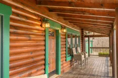 Cozy wooden cabin porch with rustic furniture, green trimmed doors, and quaint lantern-style lights.