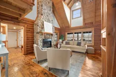 Spacious log cabin living room with high ceilings, large windows, stone fireplace, and comfortable furnishings.