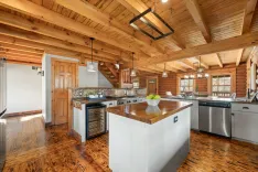 Spacious kitchen in a log cabin with stainless steel appliances, wooden ceilings, and hardwood floors.