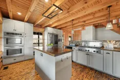 Rustic kitchen interior with wood beam ceiling, hardwood floors, white cabinets, stainless steel appliances, and a center island with a wooden countertop.