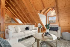 Cozy wooden attic living room with stone fireplace wall, comfortable furniture, and large windows letting in natural light.
