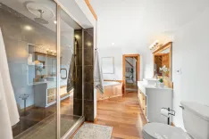 Spacious modern bathroom interior with glass shower stall, free-standing tub, double sink vanity, large mirror, and wooden accents.