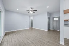 Spacious empty room with light blue walls, hardwood floors, a ceiling fan, recessed lighting, and multiple doors.