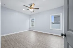 Empty room with light grey walls, hardwood floors, a ceiling fan, and a window with a view of the outside sky.