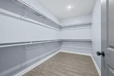 Empty walk-in closet with white wire shelving on blue painted walls and wood flooring.