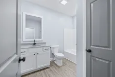 Modern bathroom interior with white cabinets, granite countertop, large mirror, toilet, and bathtub.