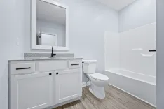 Modern bathroom interior with a white vanity, granite countertop, large mirror, toilet, and bathtub.