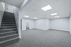 Interior of a modern office space with carpeted floors, white walls, fluorescent lighting, and a staircase to the left.