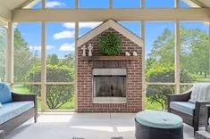 Sunlit enclosed patio with a brick fireplace, comfortable seating, and a view of the greenery outside.